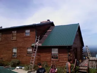 Green metal roof going on a two story log home with ladders set in Kanosh