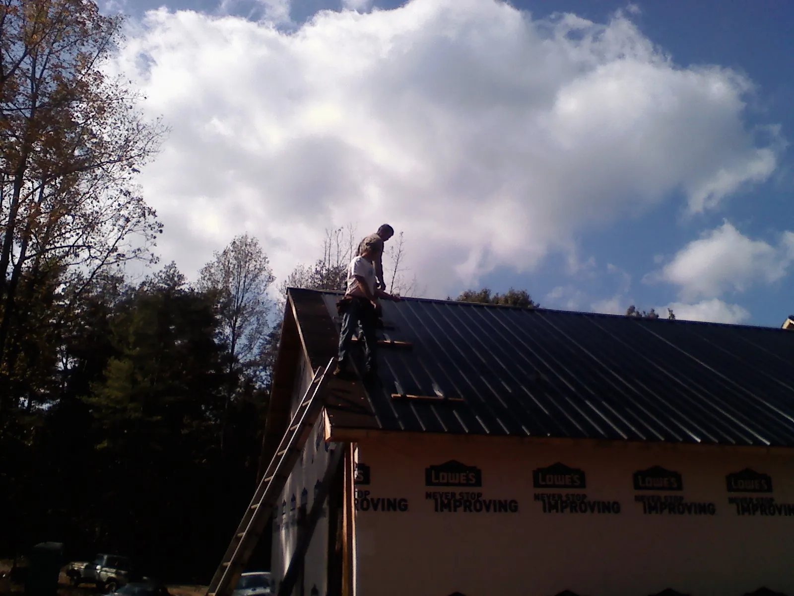 Roofer fastening dark metal panels high against a cloudy sky, from a Roof Inspection job in Kanosh